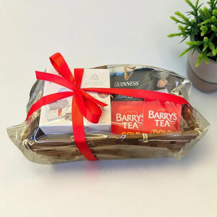 Gift basket wrapped in cellophane with a red ribbon, holding Guinness caramels and Barry's Tea