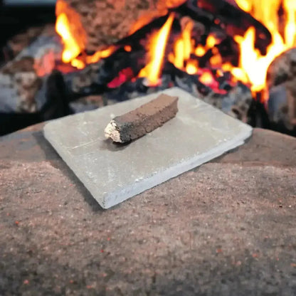 One turf incense sod with a burnt, ashy end on a grey slate, with a fire in the background