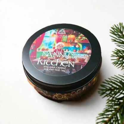 Nanny's Kitchen soy wax candle tin beside a pine branch