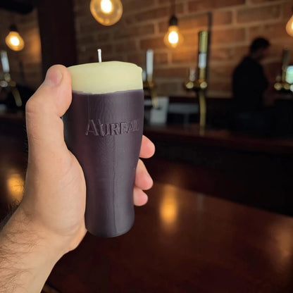 Hand holding a pint of stout candle marked Aureal in a pub