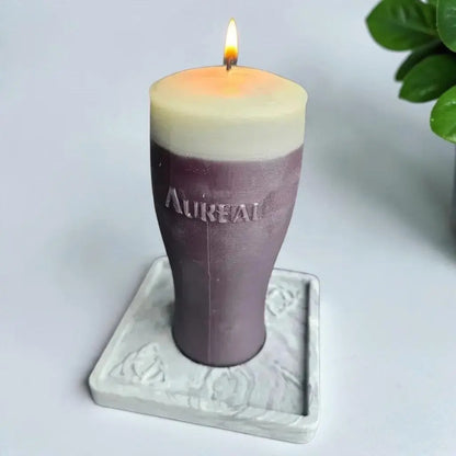 Lit pint of stout candle with a cream top and Aureal on the glass, on a square marble effect base