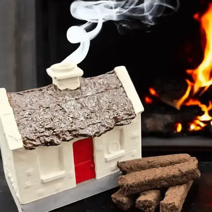 White cottage burner with smoke rising from the chimney, turf sods beside it and a fire behind